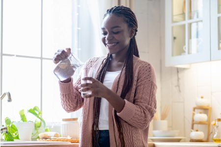 A woman in a pink sweater is pouring water into a glass